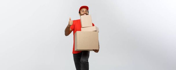 Delivery Concept - Portrait of Happy African American delivery man holding box packages and showing thumps up. Isolated on Grey studio Background. Copy Space. - Фото, изображение