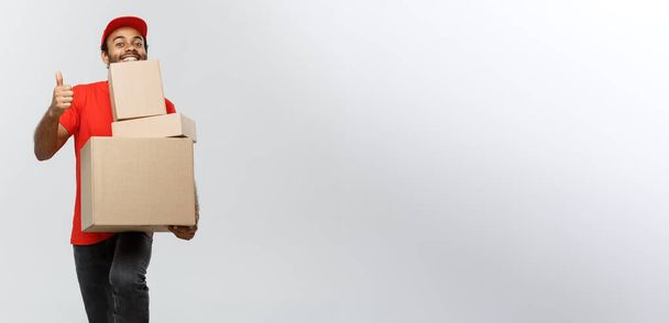 配信のコンセプト - アフリカ系アメリカ人の幸せ配達人箱のパッケージを押しながらサンドバッグを現しての肖像画。灰色スタジオ背景に分離されました。コピー スペース. - 写真・画像