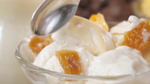 Ένα κουταλάκι του γλυκού βουτηγμένο σε λευκό παγωτό με φέτες μάνγκο. - Πλάνα, βίντεο
