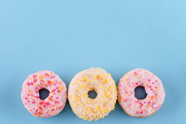 pink and yellow spricled  donuts on a blue background Space for text - Фото, изображение