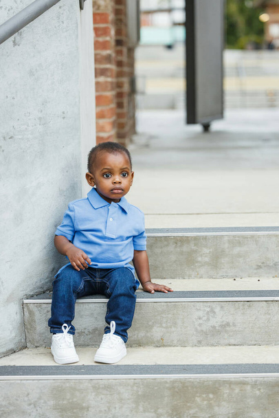 A cute one year old toddler almost preschool age African-American boy with big eyes sitting on city steps - Foto, immagini