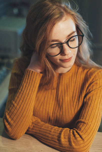 Close-up portrait of a redheaded woman wearing glasses sitting at home. Beautiful girl. Businesswoman portrait. - Фото, изображение