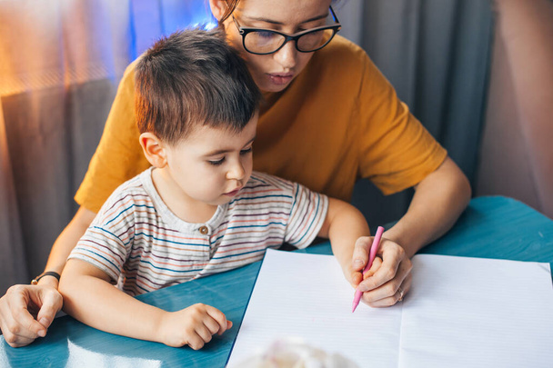 Portrait of mother and son sitting at desk holding hands drawing together. Homeschooling, distant education. Mum parent spend time with son at home preschool - Photo, image