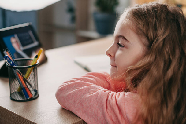 Biała dziewczyna studiuje online z tabletem siedzącym w domu odwracając wzrok. Edukacja, kształcenie na odległość, nauka w domu podczas kwarantanny - Zdjęcie, obraz