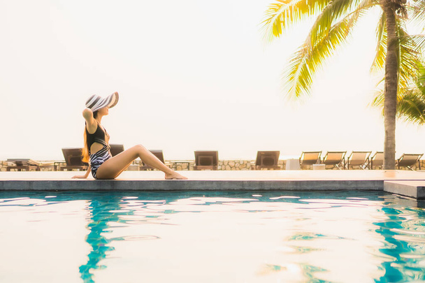 Retrato hermosa mujer asiática joven relajarse alrededor de la piscina al aire libre en el complejo hotelero con palmera al atardecer o al amanecer para vacaciones de ocio - Foto, Imagen