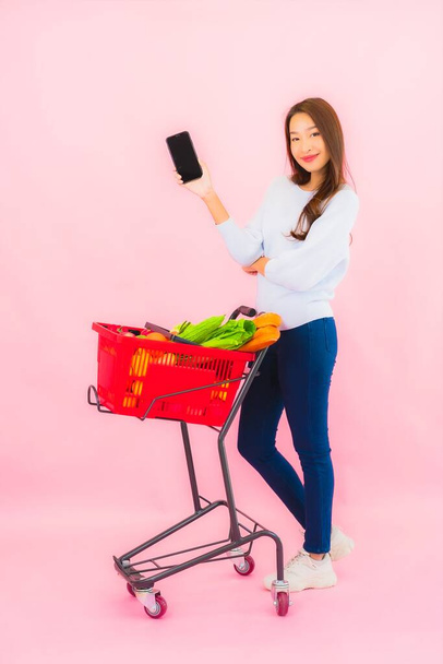 Portret mooie jonge aziatische vrouw met fruit groente en kruidenier in mand op roze geïsoleerde achtergrond - Foto, afbeelding