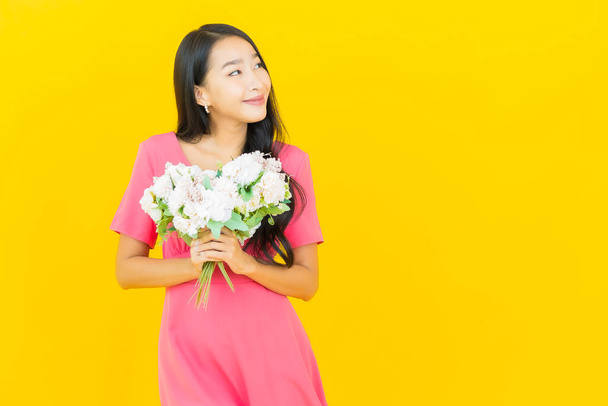 Portrait beautiful young asian woman smile with flower on yellow color background - Фото, изображение