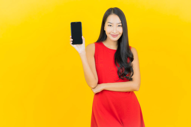 ポートレート美しいです若いですアジアの女性笑顔とともにスマートフォン上の黄色の色の背景 - 写真・画像