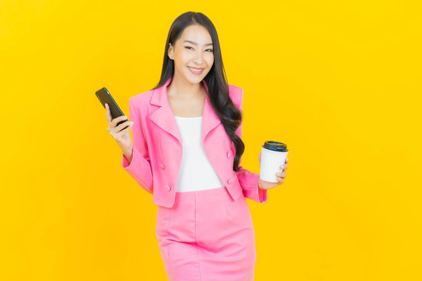 Портрет красивая молодая азиатская женщина улыбка со смартфоном на желтом фоне - Фото, изображение