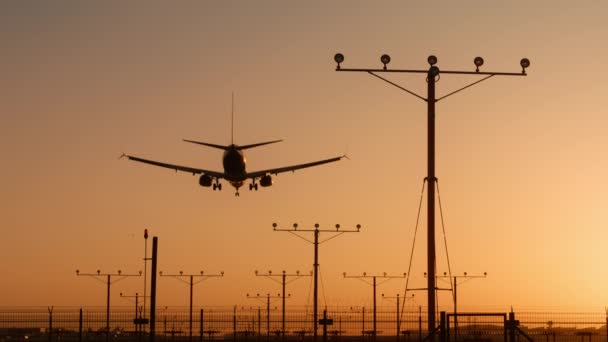 Letadlo letící nad hlavou, přistávající na letišti při západu slunce nebo při východu slunce, záběr RED kamery - Záběry, video