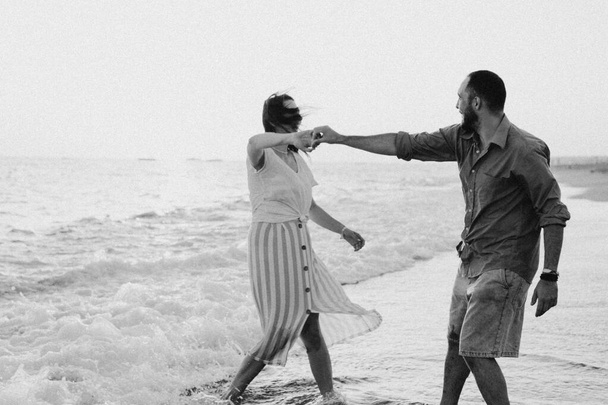 Foto en blanco y negro. Joven pareja romántica bailando girando por el mar. - Foto, Imagen