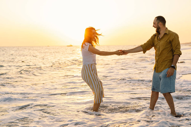 Young romantic couple dancing turning around by sea. Seascape at sunset with beautiful sky - Foto, imagen