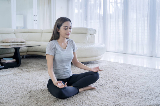 自宅のリビングルームでヨガを練習しながら瞑想をする若い女性 - 写真・画像