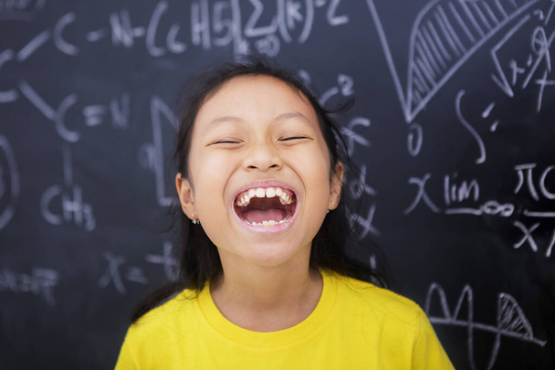 Female elementary school student laughing in the classroom while standing with doodles background - Φωτογραφία, εικόνα
