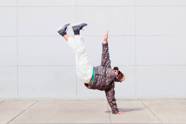 Young man wearing sweater while doing hip hop dance with handstand pose - Valokuva, kuva