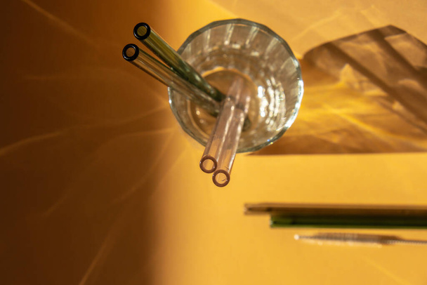 Многоразовые стеклянные соломинки в стекле с водой на бежевом нейтральном фоне Экологичный набор соломинки для питья с чистящей щеткой. Отходы, концепция без пластика - Фото, изображение