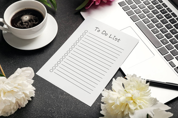 Blank to do list, pen, laptop, cup of coffee and peony flowers on dark table - Фото, изображение