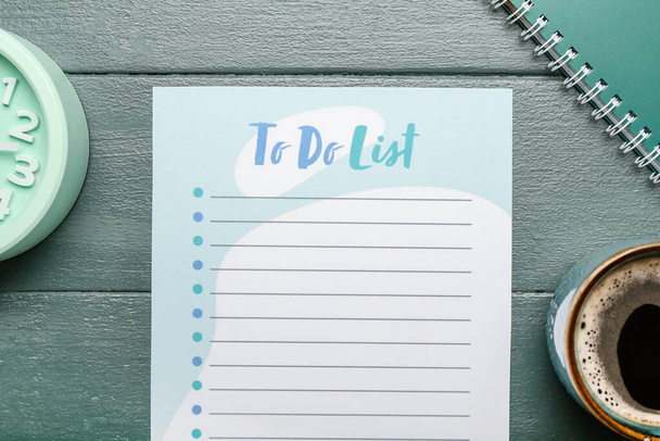 Blanco te doen lijst, wekker, notebook en kopje koffie op kleur houten achtergrond - Foto, afbeelding