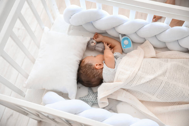 Cute little child with toy and baby monitor sleeping in crib - Valokuva, kuva