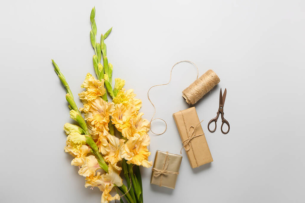 Beautiful gladiolus flowers, gift boxes, rope and scissors on grey background, closeup - Foto, Imagen