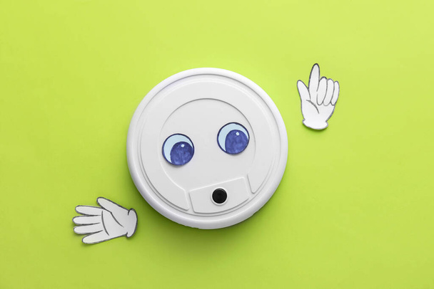 Modern robot vacuum cleaner with drawn eyes and paper hands on green background - Fotografie, Obrázek