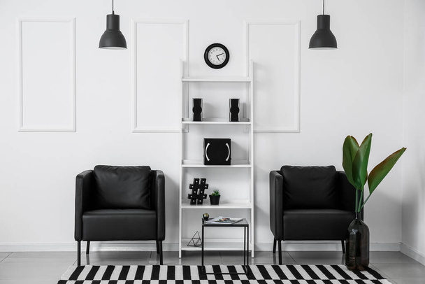 Стильный интерьер комнаты с креслами, полкой и современными динамиками возле белой стены - Фото, изображение