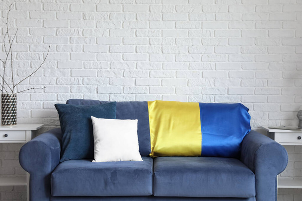 Blue sofa with flag of Ukraine and tables near white brick wall - Zdjęcie, obraz