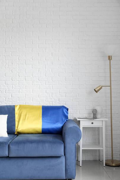 Ukrayna bayrağı taşıyan mavi kanepe, masa ve lamba beyaz tuğla duvarın yanında. - Fotoğraf, Görsel