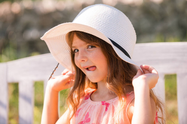 Funny kids face with tongue. Portrait of funny child girl in summer park. Face close up of cute teen girl outdoor. Cute little girl swinging on the meadow in summer day. - 写真・画像