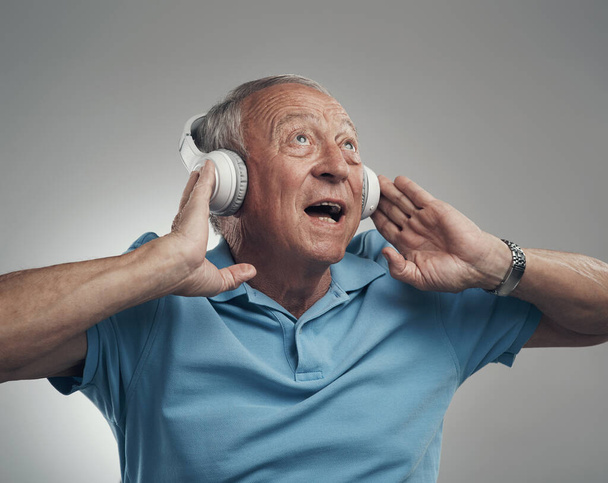 Αυτό το τραγούδι ποτέ δεν ακούστηκε καλύτερα. Φωτογραφία ενός ηλικιωμένου άνδρα που φοράει ακουστικά και ακούει μουσική σε στούντιο σε γκρι φόντο. - Φωτογραφία, εικόνα