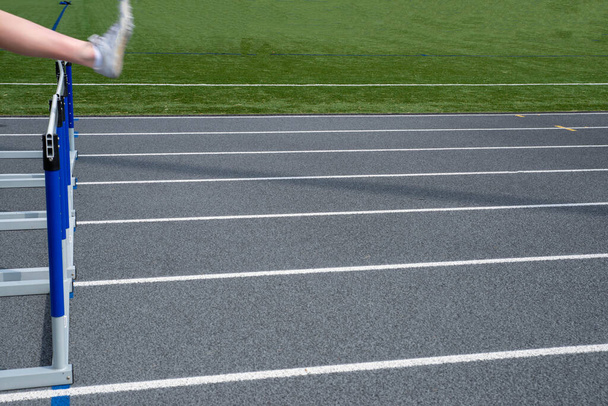 ein Fuß zeigt Bewegung, wenn er über eine Hindernis außerhalb der Mitte springt, die auf einer Leichtathletikbahn mit in natürlichem Licht mit Kopierraum gezeichneten Fahrbahnmarkierungen läuft - Foto, Bild