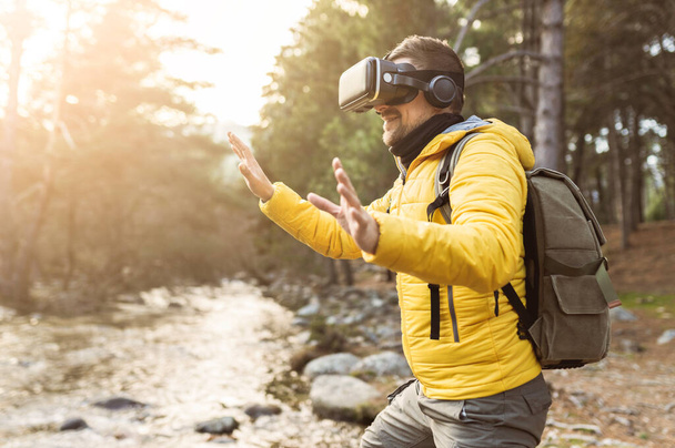 backpacker man in the forest with virtual reality headset looking directly and trying to touch something with his hand - metaverse concept - - Foto, Imagem