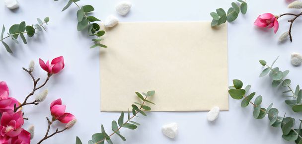 Pink magnolia flowers on twigs, fresh eucalyptus leaves. Blank pink card with grey envelope. Wood word love. Copy-space, place for greeting text. Chinese new year. Top view, off white background. - Foto, Imagem