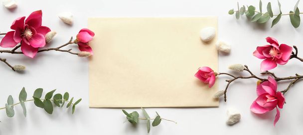 Pink magnolia flowers on twigs, fresh eucalyptus leaves. Blank pink card with grey envelope. Wood word love. Copy-space, place for greeting text. Chinese new year. Top view, off white background. - Zdjęcie, obraz