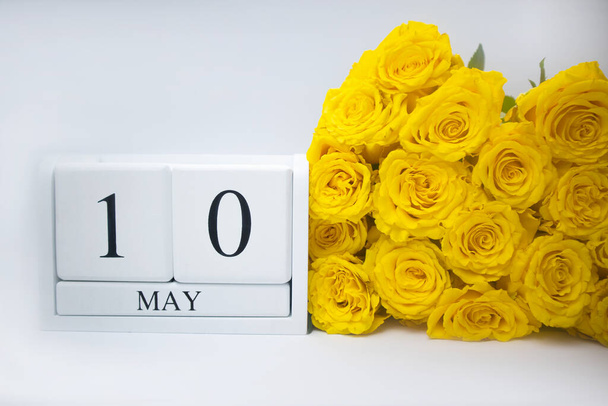 10 Mayıs beyaz ahşap bir takvimde ve sarı bir buket gül yan yana yatar. - Fotoğraf, Görsel