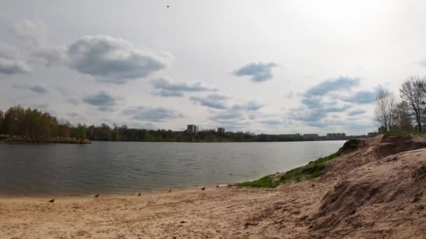 Timelapse of moving clouds. Fast-paced footage of clouds over a lake in northern Europe. Beach near the lake. People are walking along the beach. Panoramic timelapse of a landscape in motion.  - Felvétel, videó
