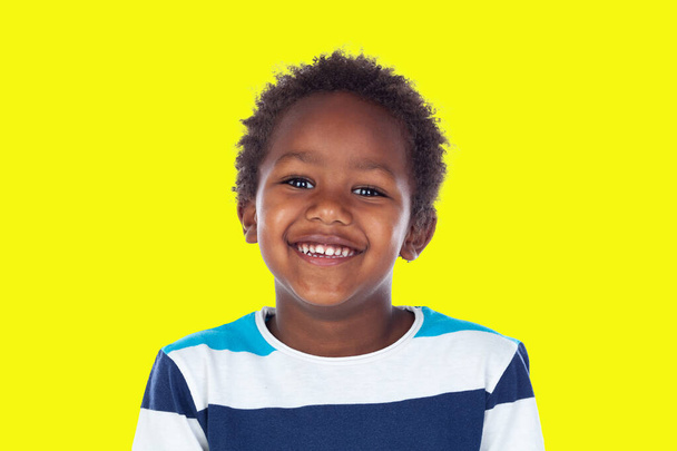 Enfant africain avec un t-shirt regardant la caméra et riant isolé sur un fond jaune  - Photo, image