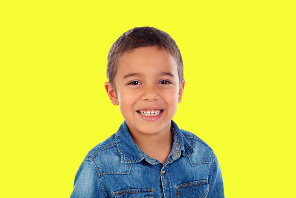 Latin child with denim shirt looking at camera and laughing isolated on a yellow background  - Fotografie, Obrázek