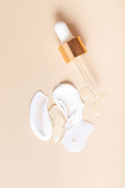 Top drops and smears of cream cosmetics with a pipette on a beige background. - Photo, image