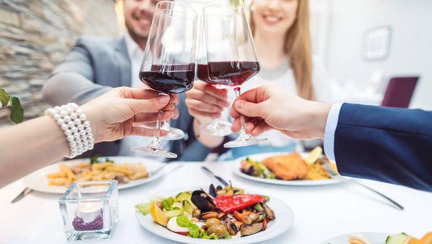 Close-up on hands of patrons in restaurant with glasses of red wine - 写真・画像