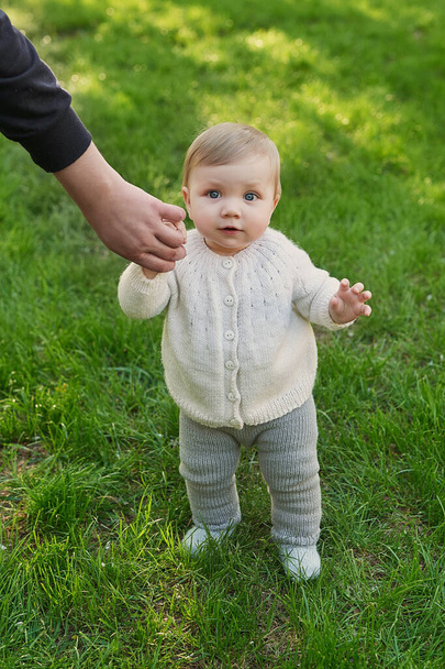 Lachende kleine jongen op gras in het park. Dag van de kinderbescherming. Wereldkinderdag. Vader houdt kind met de hand vast. Eerste stappen. - Foto, afbeelding