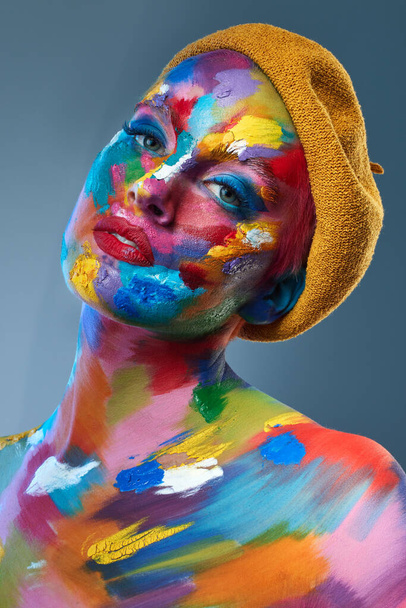 Hayat bir kutu pastel boyayı kullanmaktan ibarettir. Yüzünde çok renkli boya ve kafasında Fransız şapkasıyla poz veren genç bir kadının stüdyo fotoğrafı.. - Fotoğraf, Görsel