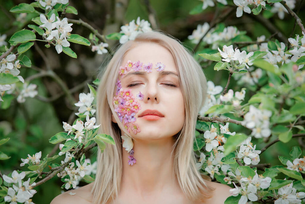 Красива жінка з пелюстками квітів на обличчі навколо квітучої яблуні
 - Фото, зображення