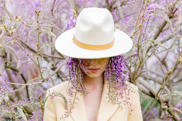 Beautiful woman with flowers petals on face around blooming wisteria tree branches - Fotografie, Obrázek