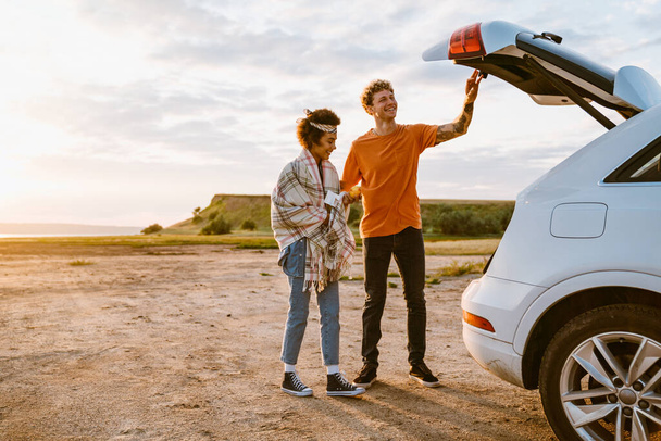 Young multiracial couple smiling together while standing by car during trip - Foto, Imagem