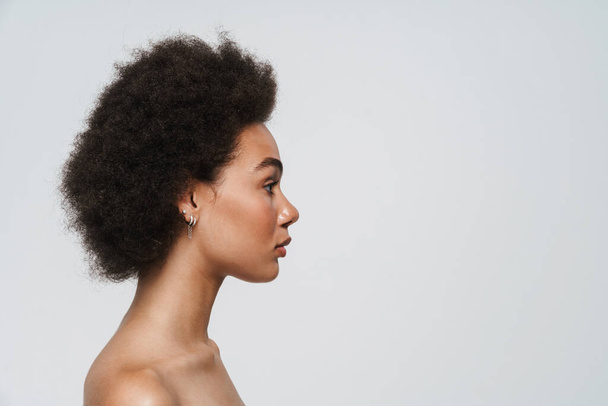 Fekete félmeztelen nő néz félre, miközben pózol profil elszigetelt fehér háttér - Fotó, kép