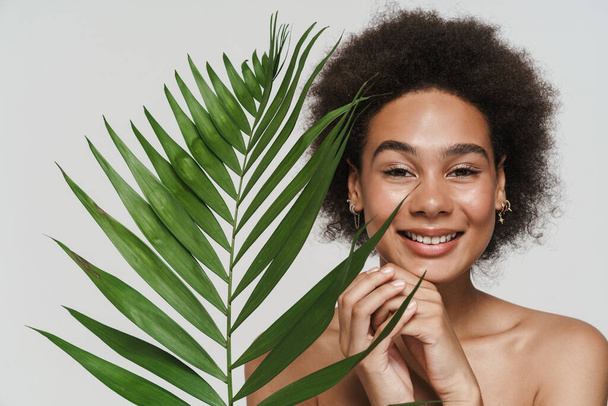 Black shirtless woman smiling while posing with green leaf isolated over white background - Foto, afbeelding