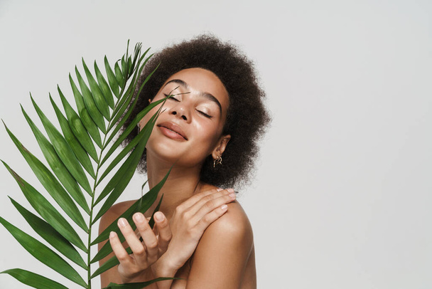Black shirtless woman smiling while posing with green leaf isolated over white background - Zdjęcie, obraz