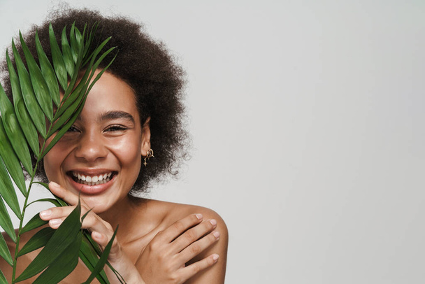 Black shirtless woman laughing while posing with green leaf isolated over white background - Foto, afbeelding