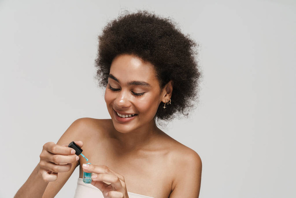Black curly brunette woman smiling while applying nail polish isolated over white background - Foto, Imagem